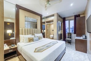 Quarto de hotel com uma cama grande, uma escrivaninha com cadeira, um espelho e vista para a cidade pela janela.