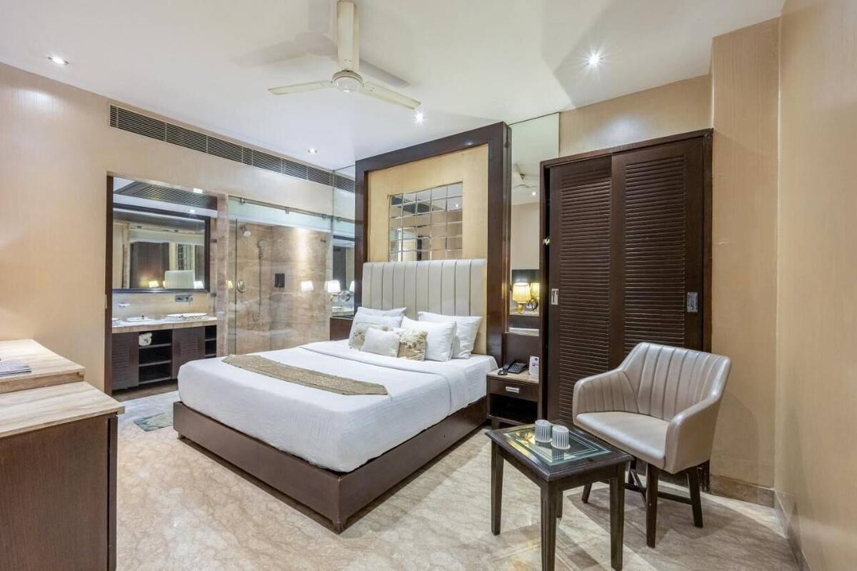 Quarto de hotel moderno com uma cama grande, escrivaninha, cadeira, espelho e guarda-roupa.