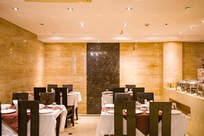 Un restaurant aux murs de marbre, aux tables recouvertes de nappes blanches et doté d’un espace buffet.