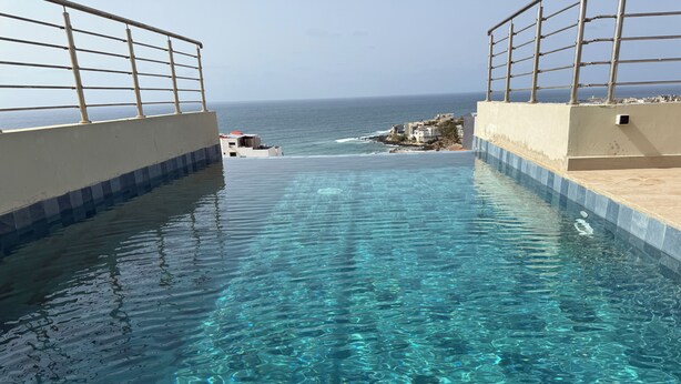 A clear pool with a view of the ocean and a rocky coastline. - Luxury apartment with rooftop, games room, 5 min from the beach (Dakar)