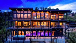 A multi-story modern house with large windows, a hot tub, and outdoor seating. - LUXURY NEW CONSTRUCTION! Mountain Horizon–Pool, Spa, Sports Court, Golf, Views (Pigeon Forge)