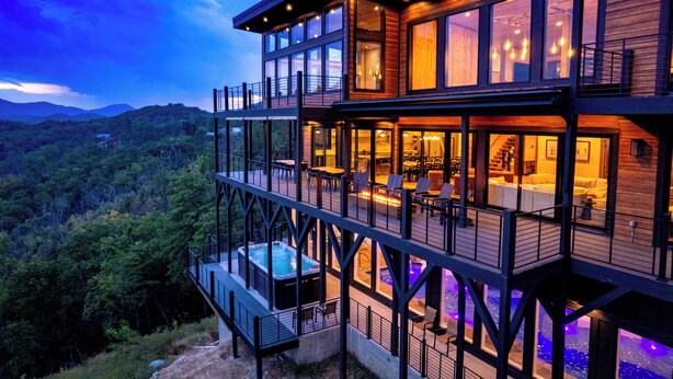 A multi-level wooden house with a hot tub, outdoor seating, and large windows. - LUXURY NEW CONSTRUCTION! Mountain Horizon–Pool, Spa, Sports Court, Golf, Views (Pigeon Forge)