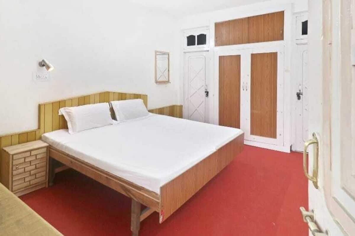 Une chambre avec un lit en bois, une moquette rouge et des murs blancs.
