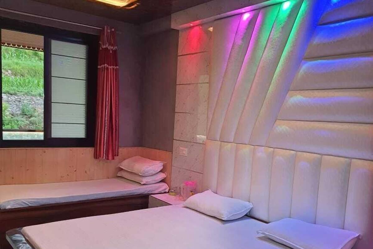 Une chambre avec un grand lit, deux petits lits, une fenêtre donnant sur un paysage verdoyant et un plafond doté d’un éclairage aux couleurs vives.
