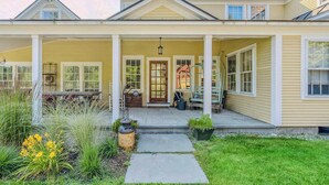 A two-story house with a covered porch, a front door, and a small garden area with plants and a pathway. - Saskadena Lodge with Game Room, near Ski Hill (Pomfret)
