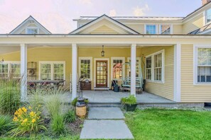 A two-story house with a covered porch, a front door, and a small garden area with plants and a pathway.