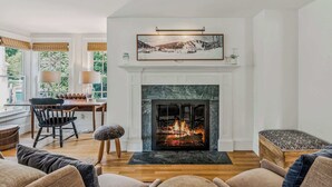 A living room with a fireplace, wooden furniture, and a painting above the mantel. - Saskadena Lodge with Game Room, near Ski Hill (Pomfret)
