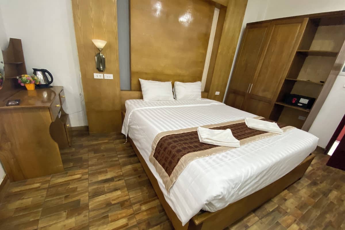 Habitación de hotel ordenada con una cama de madera, un escritorio con un hervidor y un armario.