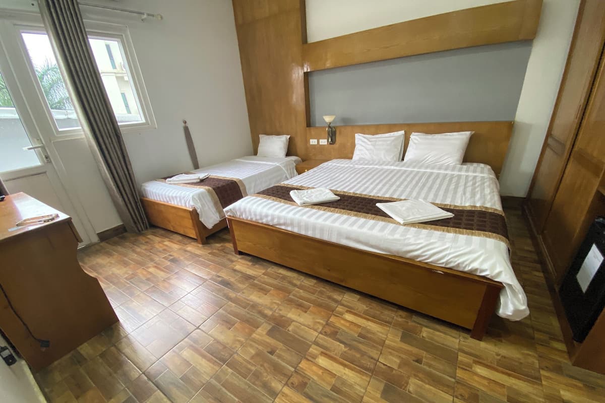 Habitación de hotel con una cama grande, dos camas más pequeñas, piso de madera, un escritorio y una ventana con cortinas.