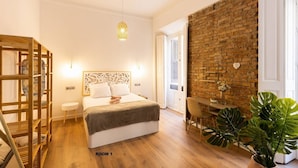 Une chambre à coucher avec un lit, des tables de chevet, un luminaire suspendu, un mur en briques et une plante en pot.