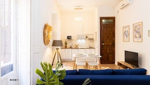 Une pièce comprenant un canapé bleu, une table à manger avec des chaises, un coin cuisine et un téléviseur.