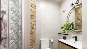 Une salle de bain avec une douche à parois de verre, des toilettes, un lavabo avec un miroir et une plante en pot.