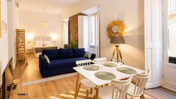 Un salon moderne avec un canapé bleu, une table à manger et quatre chaises, ainsi qu’une lampe.