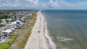 An aerial view of a coastal residential area with houses along the beach, a pier extending into the ocean, and a clear sky. - True North - Ocean Bliss Retreat in Kure Beach (Kure Beach)