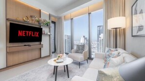 Ein modernes Wohnzimmer mit einem großen Flachbildfernseher, der das Netflix-Logo zeigt, einer Couch, einem Couchtisch und Blick auf die Stadt durch große Fenster.