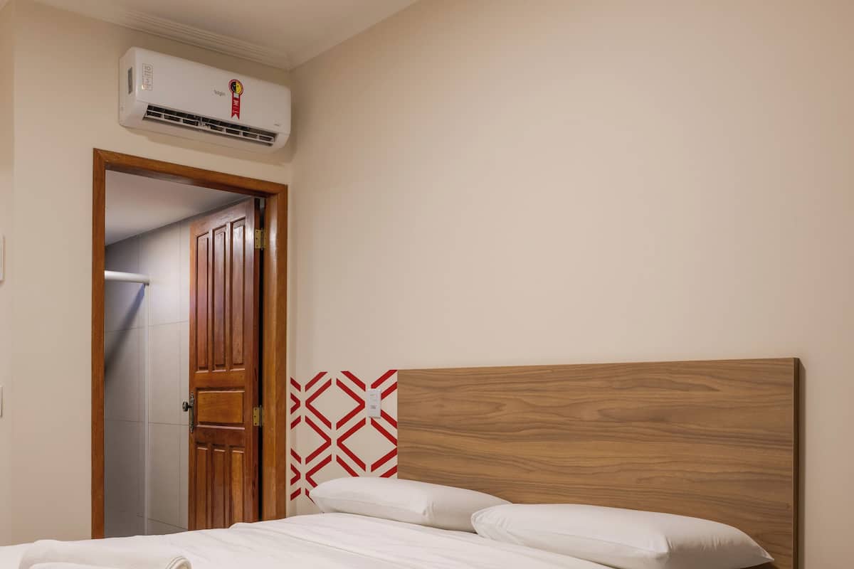 A neatly made bed with white linens, a wooden headboard, and a red and white geometric-patterned wall hanging.