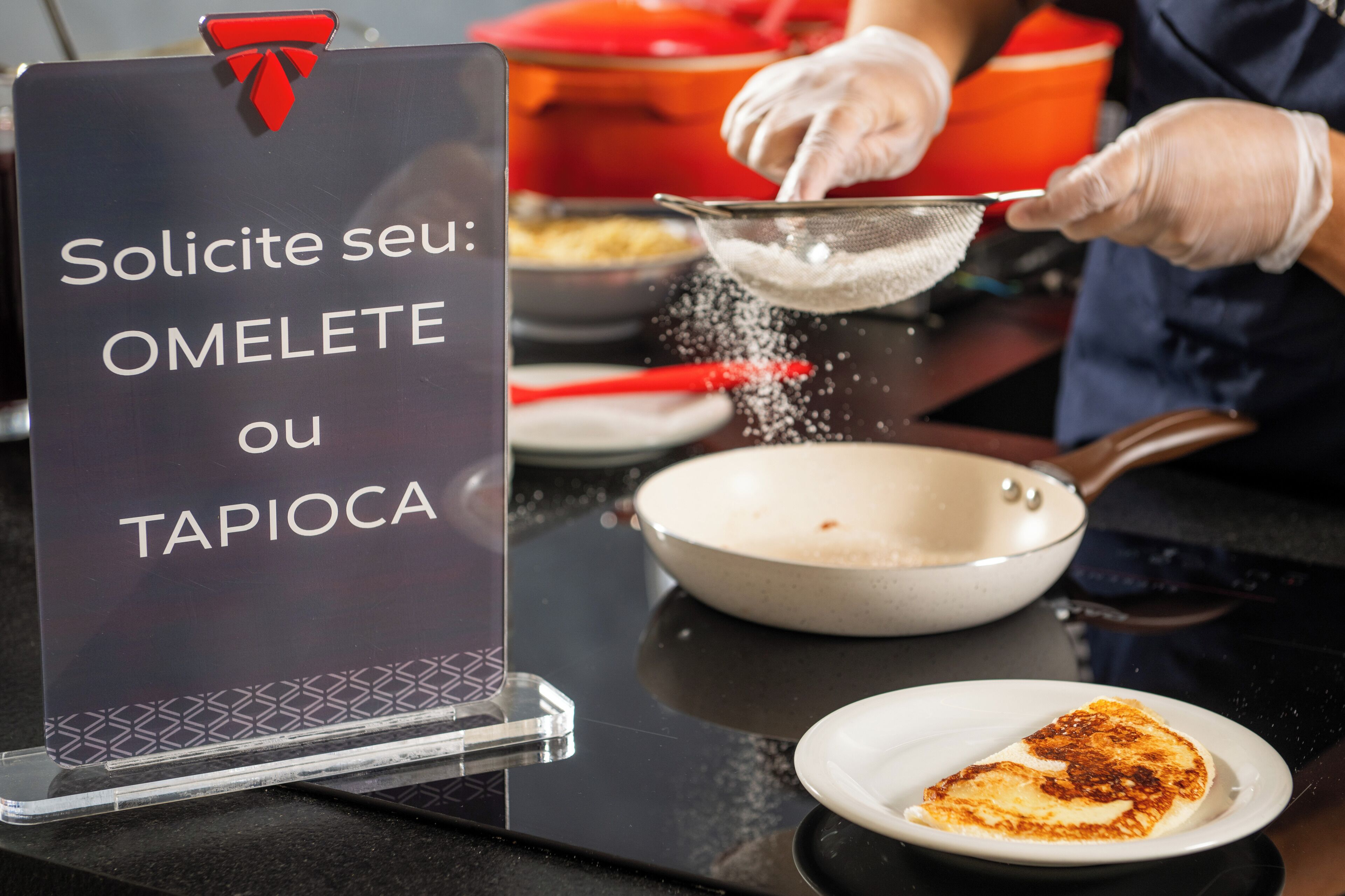 A sign with text in a foreign language, a person wearing gloves, a frying pan, and a plate with food.