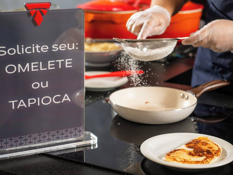 A sign with text in a foreign language, a person wearing gloves, a frying pan, and a plate with food.