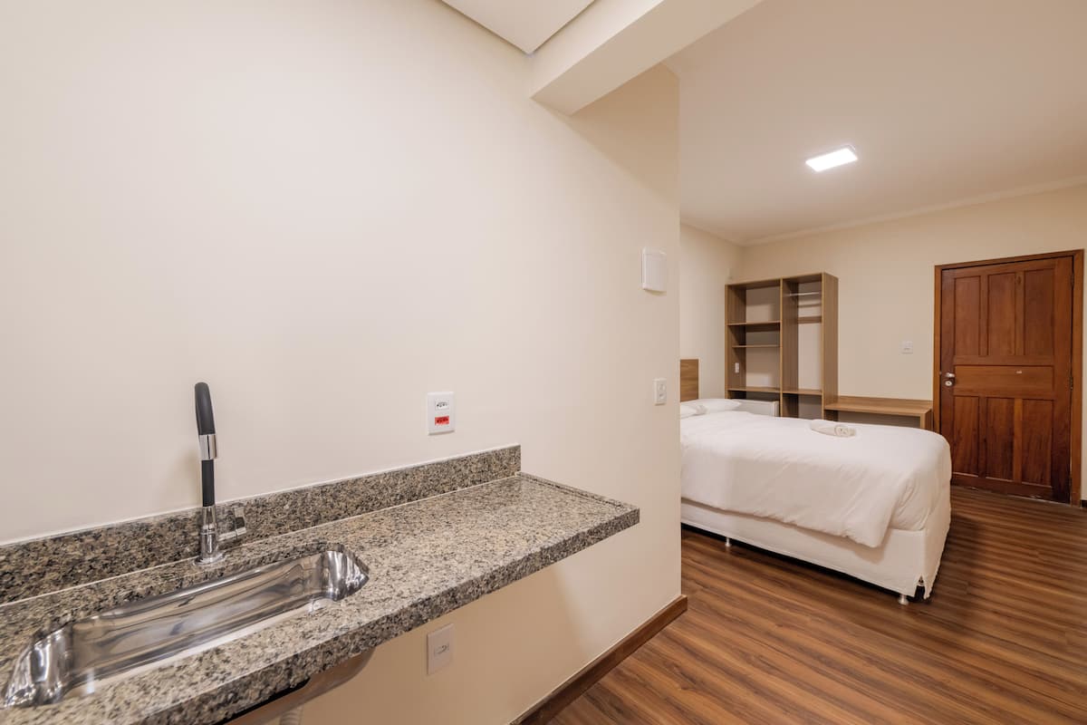 A hotel room with a granite countertop sink, a bed, a wooden door, and a built-in shelving unit.