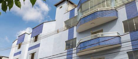 A multi-story building with a blue-tiled facade, a visible entrance, and a parked car.
