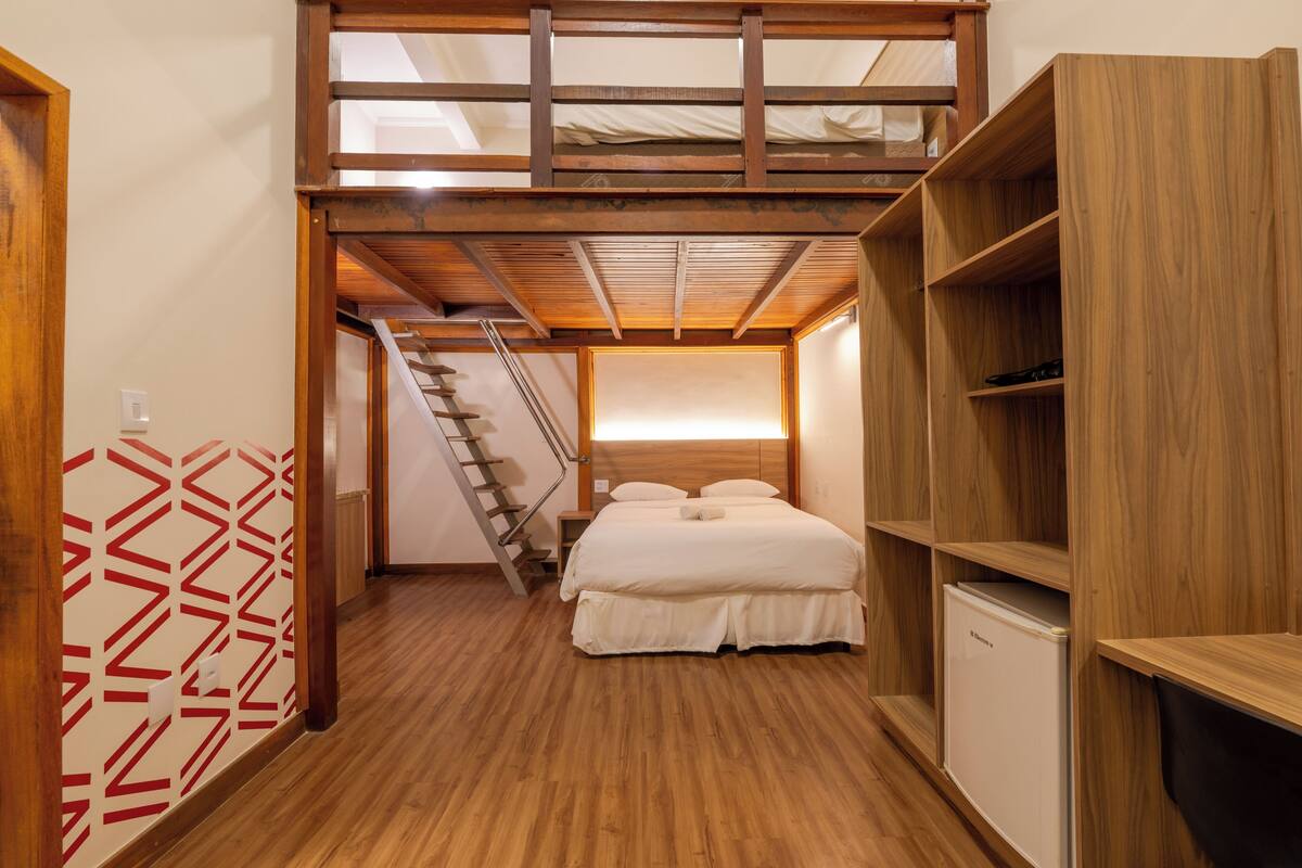 A bedroom with a bunk bed, wooden flooring, a built-in wardrobe, and a staircase leading to an upper level.
