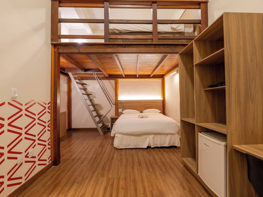 Quarto com beliche, piso de madeira, guarda-roupa embutido e escada para um andar superior.