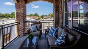 A balcony with a wicker sofa, a small table with a plant, and a view of a town.