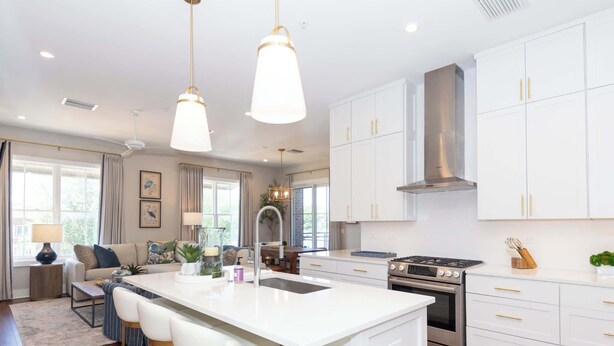 A modern kitchen with white cabinetry, a central island with bar stools, stainless steel appliances, and pendant lighting.