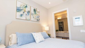 A bedroom with a bed, a nightstand, a lamp, a mirror, and abstract wall art.