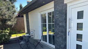 Une terrasse avec une table et des chaises, une porte blanche avec des panneaux de verre et un mur en pierre.