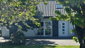 Une maison avec un toit en tuiles, une porte en verre et un petit patio aménagé avec des chaises.