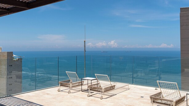 A balcony with two sun loungers and a small table, overlooking a clear blue sea with distant ships. - Apartamento SuiLoft 1313 Bello Horizonte (Santa Marta)