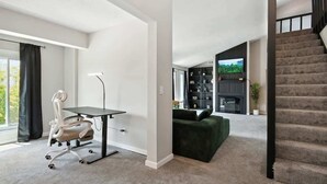 A modern living room with a desk, a green sofa, and a staircase. - Stylish 2BR Loft, Near ISU, Hospitals & Downtown (Bloomington)