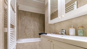 Ein Badezimmer mit einer Badewanne, einem weißen Waschtisch mit Spiegel und einem Handtuchhalter.