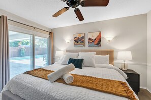 Ein Hotelzimmer mit einem großen Bett, einem Deckenventilator, zwei Wandleuchten und Blick auf einen Swimmingpool durch eine Glastür.