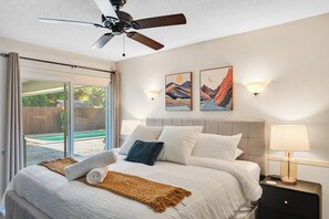 Habitación de hotel con cama, ventilador de techo, mesita de noche con lámpara y dos lámparas de pared.