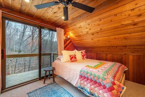 Ein gemütliches Schlafzimmer mit einem großen Fenster, einem Deckenventilator und einer farbenfrohen Bettdecke.