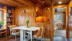 A cozy cabin interior with a wooden dining table, two chairs, a bookshelf, and a window overlooking a forest. - Mountain Dove Log Cabin Healing Retreat+Mtn Views+Walking trail (Weaverville)