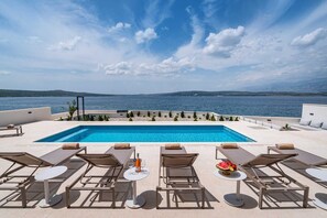 A pool area with a view of the sea, lounge chairs, and a table with a bottle and glasses. - Villa Rosa dei Venti with Pool (Novigrad)