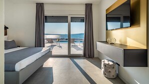 A modern hotel room with a bed, a TV, and a view of the sea.