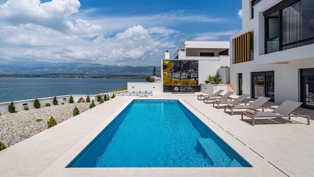 A modern pool area with a clear view of the sea and mountains in the background.