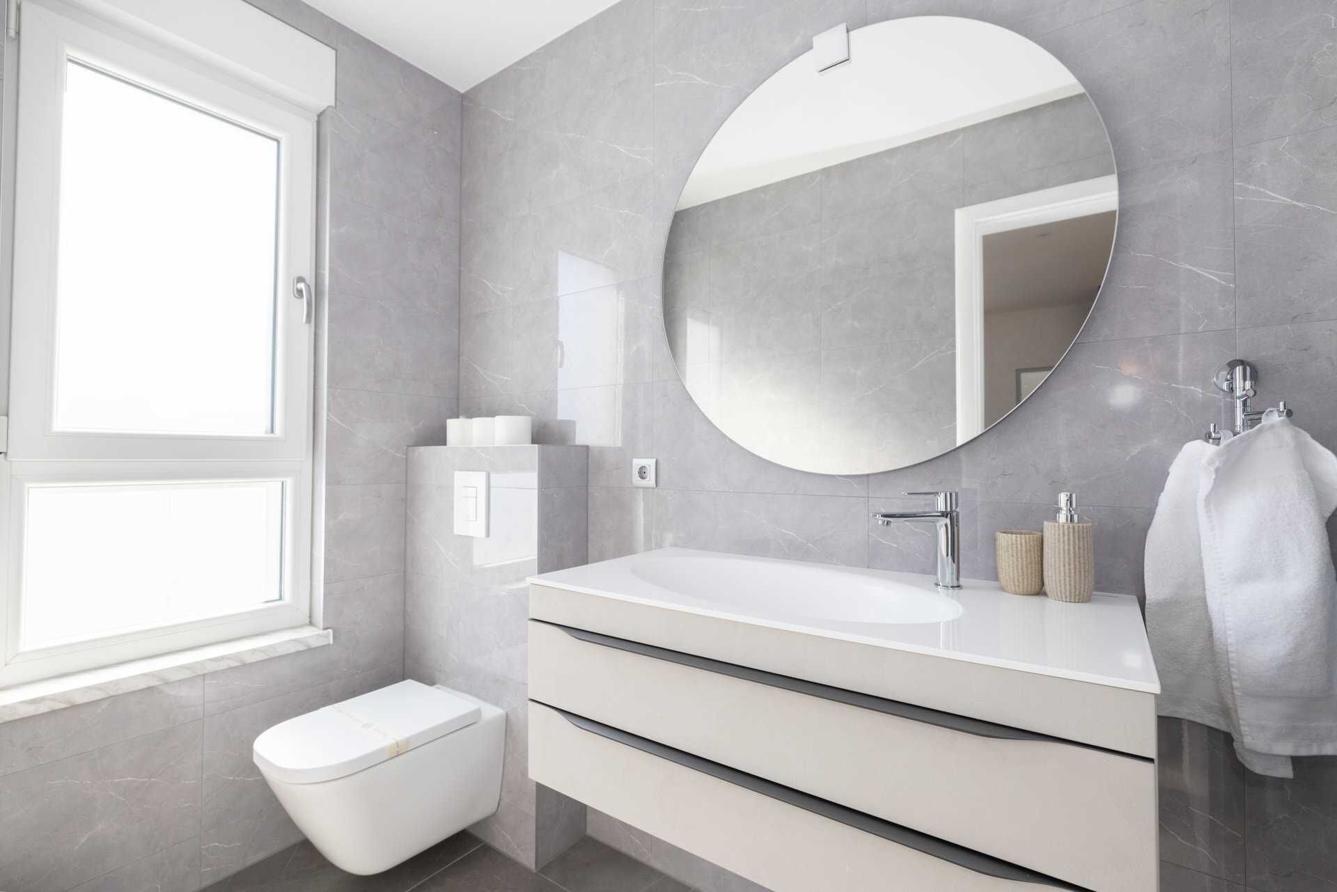 A modern bathroom with a large mirror, a white sink, and a toilet.