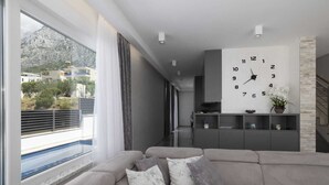 A modern living room with a grey sofa, a large wall clock, and a view of a balcony with a pool. - Villa Azulmar with Heated Pool (Makarska)