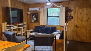 A cozy room with wooden walls, a television, a bookshelf, a sofa, and a dining table.