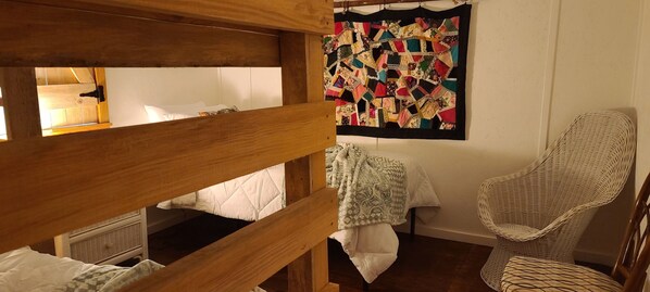 Una cama nido con colchón acolchado, una silla de mimbre y un colcha colorida en la pared.