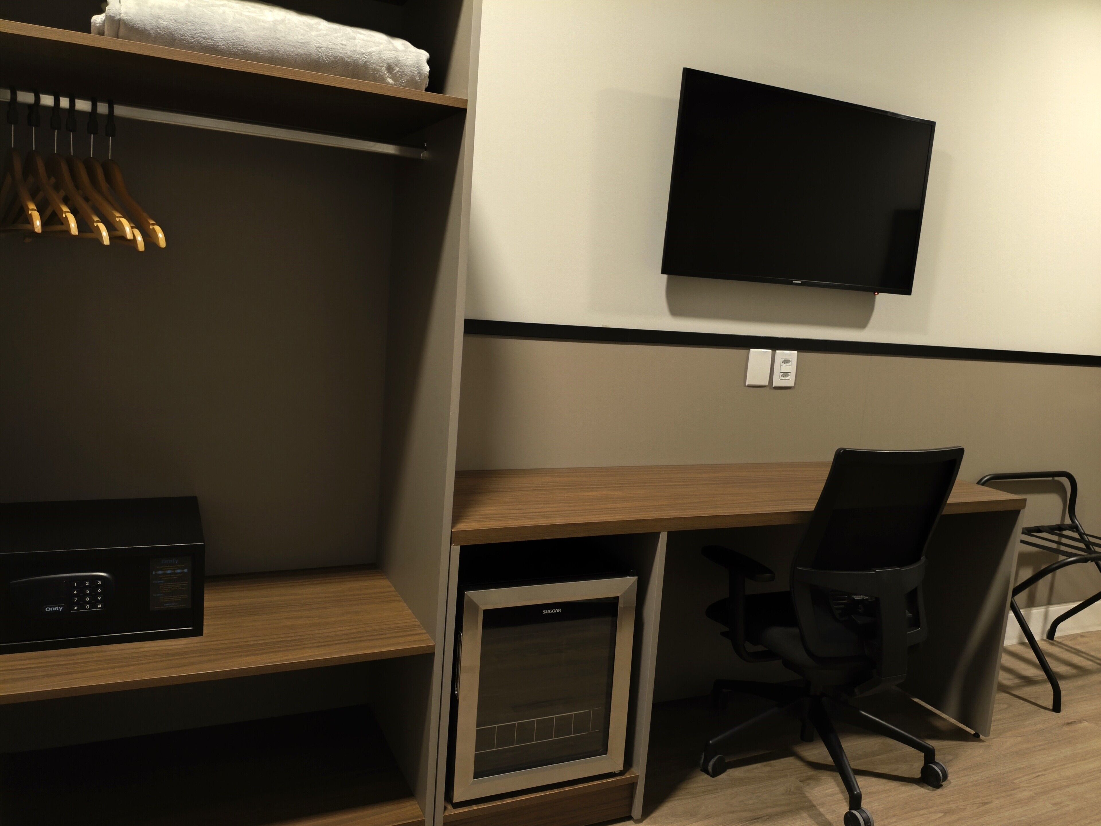 Une chambre d’hôtel équipée d’un bureau en bois, d’un fauteuil de bureau noir, d’un téléviseur fixé au mur, d’un four à micro-ondes et d’un petit four.