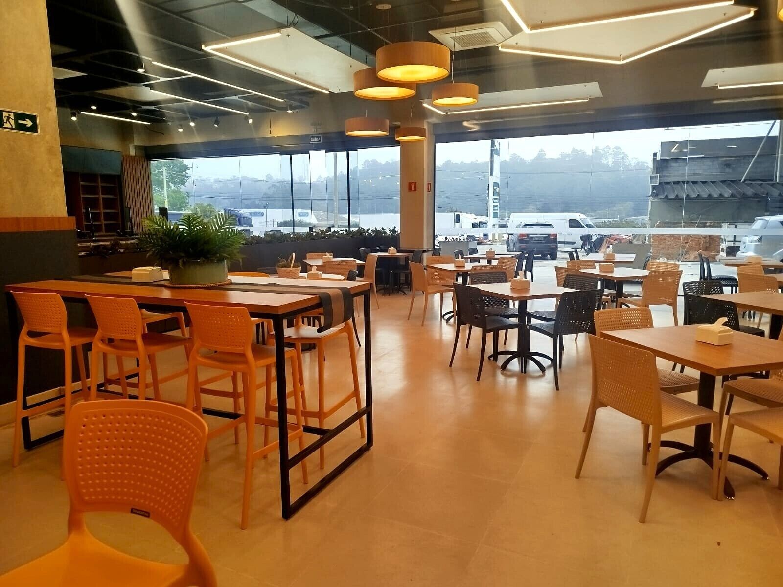 A spacious cafe with multiple seating areas, large windows offering a view of the parking lot, and a modern interior design.