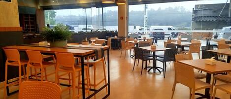 En rummelig café med flere siddeområder, store vinduer der giver udsigt til parkeringspladsen, og et moderne interiør.