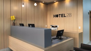 A hotel reception desk with a wooden panel wall, a sign reading "HOTEL 28", and a computer monitor.