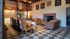 Un comedor con piso a cuadros, sillas de madera, una mesa dispuesta para una comida, una chimenea y una escalera que sube a un nivel superior.